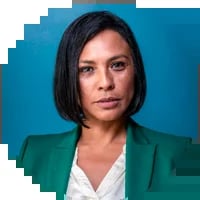 Professional headshot of a woman with black shoulder-length hair wearing a teal blazer over a white top against a blue background