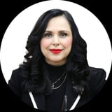 Professional headshot of a woman with long black wavy hair, red lipstick, wearing a black blazer against a white circular background