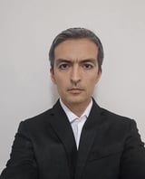 Professional headshot of a man with dark hair wearing a black blazer and white shirt against a neutral background