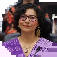 Woman wearing purple cardigan and glasses with gold hoop earrings at an event